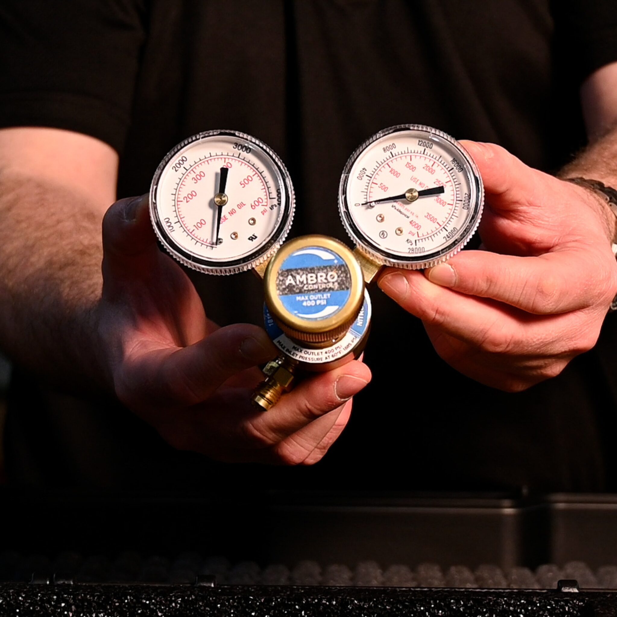 Technician holding a dual-gauge nitrogen regulator with clear PSI markings and Ambro Controls branding.